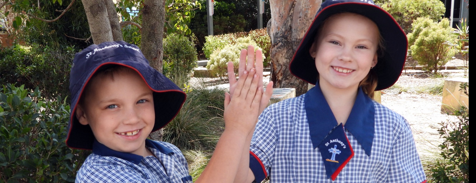 Students in school uniform outdoors engaging in a friendly high five, highlighting positive relationships, cooperation and wellbeing within the school environment